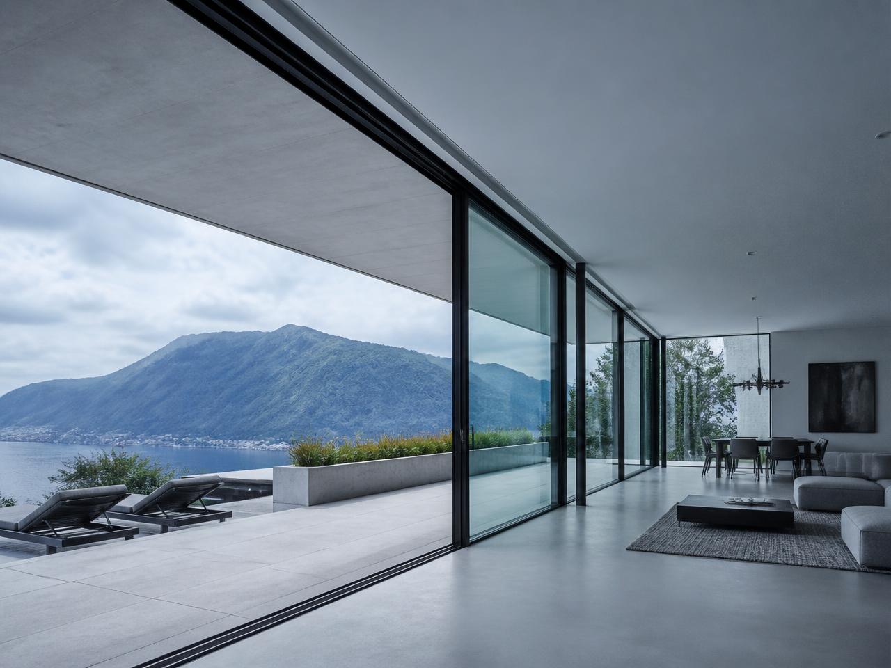 Sliding steel glass wall with ultra-slim black profiles opening onto a terrace with a distant mountain view