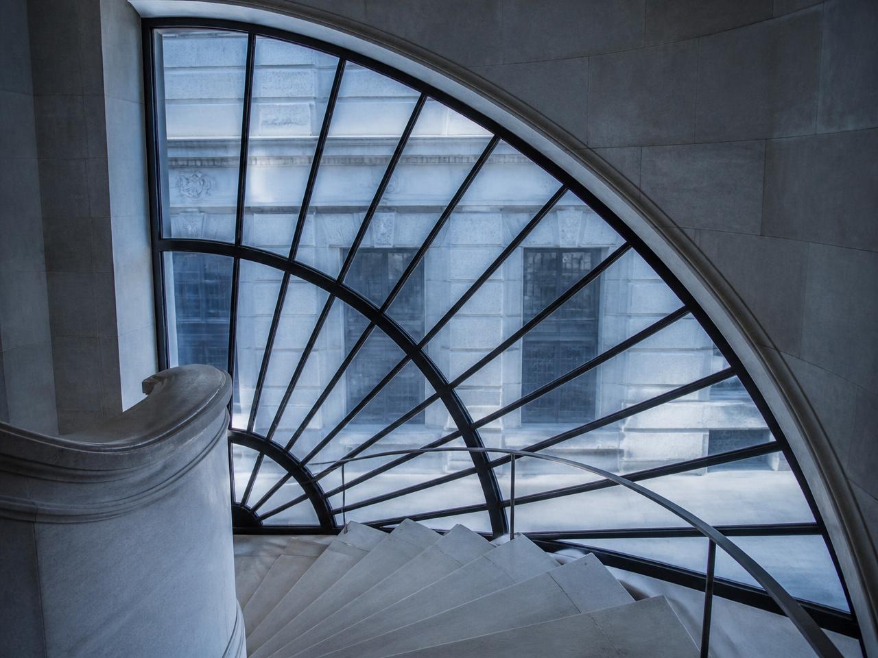 Bespoke curved steel window with radial glazing pattern in a pale stone stairwell